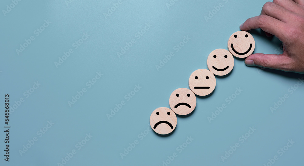 Poster Hand holding smile face which print scree on round wooden among regular and sad emotion for excellent client evaluation after customer use product and service concept.