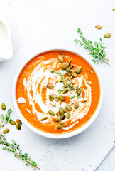 Pumpkin cream soup with pumpkin seeds, cream and thyme.. Winter or autumn healthy vegetarian food. White soup bowl on light table background. Top view
