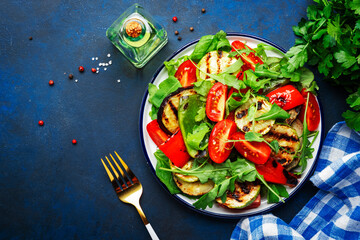 Healthy salad with grilled vegetables, paprika, zucchini, eggplant with fresh tomatoes and mixed herbs. Blue table background, top view