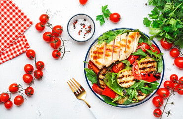 Healthy salad with grilled chicken breast fillet and vegetables: paprika, zucchini, eggplant, fresh tomatoes and mixed herbs. White table background, top view - obrazy, fototapety, plakaty