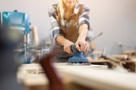 Carpenter woman professional skill using electric sander for wood in carpentry shop