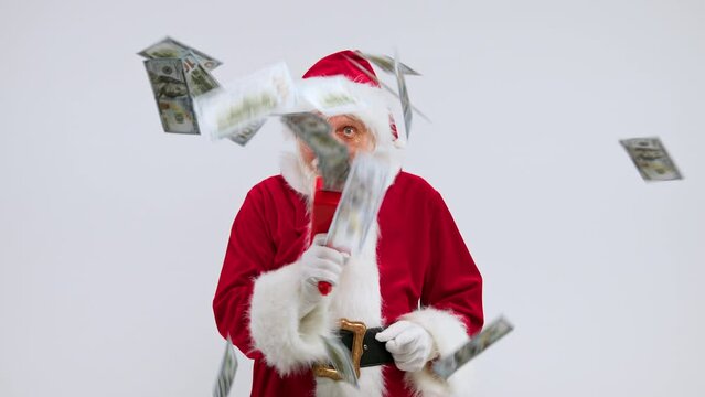 Santa Claus plays with toy gun shooting money banknotes around white studio with smile