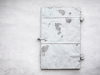 weathered metal door on old shabby painted white concrete wall. grunge background.