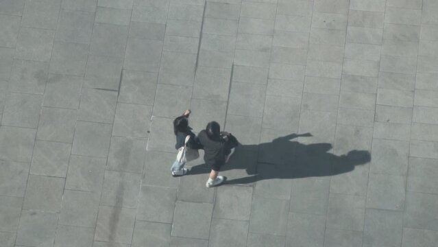 Verical aerial view of People walk cast dark shadows from sun onto concrete gray surface.