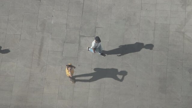 Verical aerial view of People walk cast dark shadows from sun onto concrete gray surface.