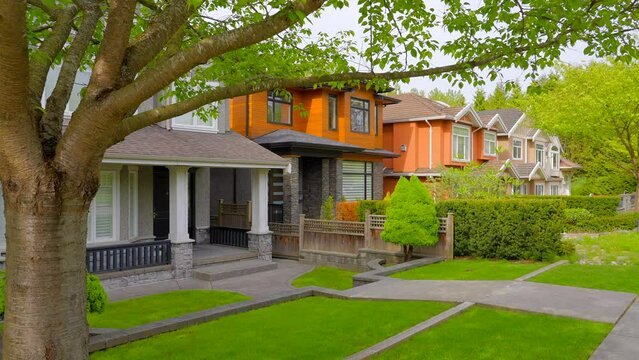 Establishing shot of two story stucco luxury house with garage door, big tree and nice spring blossom landscape in Vancouver, Canada, North America. Day time on May 2022. ProRes 422 HQ.