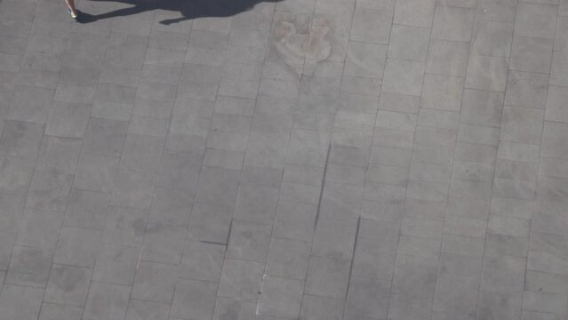 Verical aerial view of People walk cast dark shadows from sun onto concrete gray surface.