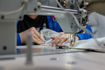 Close-up of the sewing process. Women's hands stitching beige fabric on a professional production machine in the workplace. Seamstress's hands hold textiles for making dresses or furniture paneling