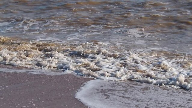 Muddy brown waves with white sea foam beat against the sandy shore