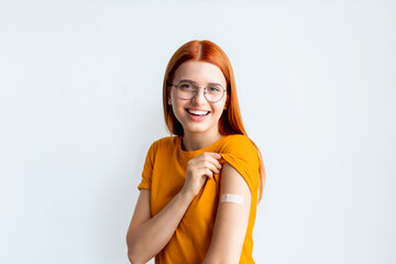 Happy young woman after vaccination showing arm with band-aids after injection standing on a white...