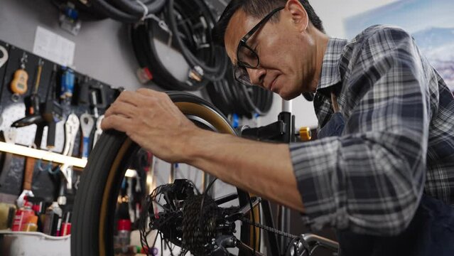 Asian senior man worker repairing and checking wheels and gears of bicycle while standing in bicycle shop