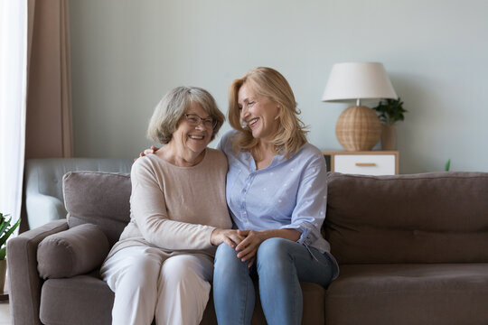 Middle-aged woman visit old mother, multi-generational family sit on sofa smile enjoy warm conversation and priceless time together. Harmony, communication between different generation relatives women