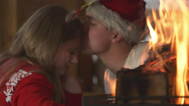 CLOSE UP: Burning flames and cute couple sharing romantic moments on Christmas. View of fireplace and young twosome in love enjoying cosy atmosphere in home living room on festive winter Evening.