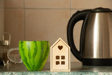A cup with the image of a watermelon stands on a table in the kitchen near a small house and a...