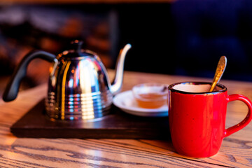 Red cup, metal kettle on a wooden dark table. Tea party in the restaurant