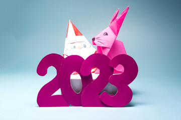 Fototapeta premium Blue background with numbers 2023, cheerful Santa claus and pink rabbit close-up