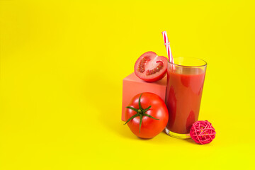 Fresh tomato juice in a transparent glass with a decor of tomatoes and salt on a yellow background.