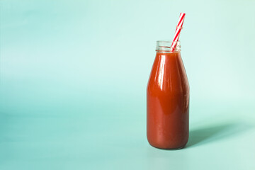 Tomato juice in a glass bottle with a red tube in natural light on a blue background.
