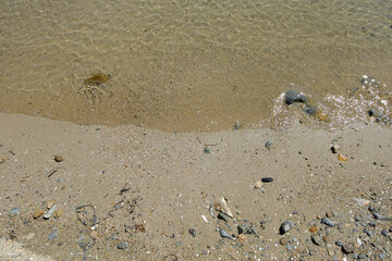 Fototapeta na wymiar Sandy seashore with clear, transparent water with sun glare