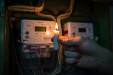 Candle shining light in the dark near electricity meter during power outage at home.  no electricity