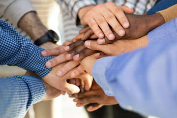 Cropped close of diverse businesspeople putting their hands on top of each other wearing casual...