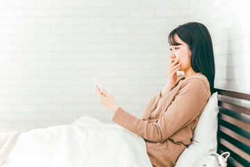 ベッドルームでスマホを見て驚く日本人女性
