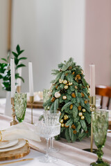 Mini Christmas tree among cutlery and dishes and stylish table setting on Christmas Eve.