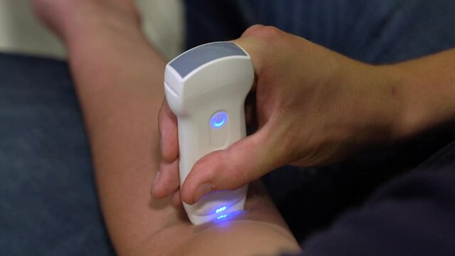 Man makes an ultrasound on his arm with a portable x-ray scanner. Man diagnoses by doppler health in hospital
