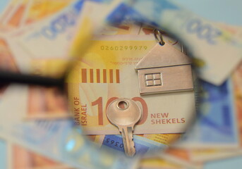 Israeli shekel banknotes and a key with a house keychain, a magnifying glass. Concept: buying real estate in Israel, renting a house, mortgage loan. - obrazy, fototapety, plakaty