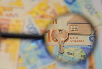 Israeli shekel banknotes and a key with a house keychain, a magnifying glass. Concept: buying real estate in Israel, renting a house, mortgage loan. - obrazy, fototapety, plakaty