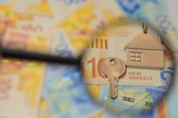 Israeli shekel banknotes and a key with a house keychain, a magnifying glass. Concept: buying real...