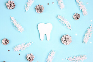 White tooth surrounded by white fir branches and cones on blue background.