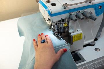 person using a machine. White female hands hold the fabric when sewing on a professional sewing machine