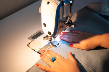 White female hands hold the fabric when sewing on a professional sewing machine