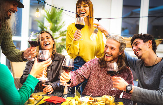 Young people toasting red wine at dinner party garden - Trendy friends having fun together at restaurant winery bar out side - Happy hour life style concept on bright warm filter with string lights