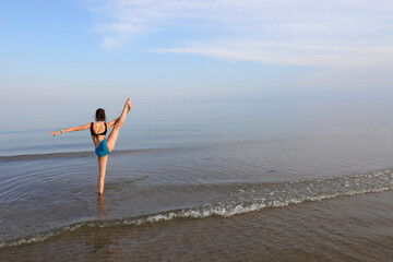 slender athletic girl performs gymnastic exercises on the sea near the shore