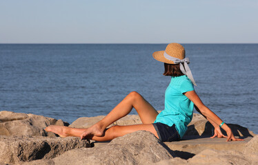 girl with straw hat on the rocks by the sea