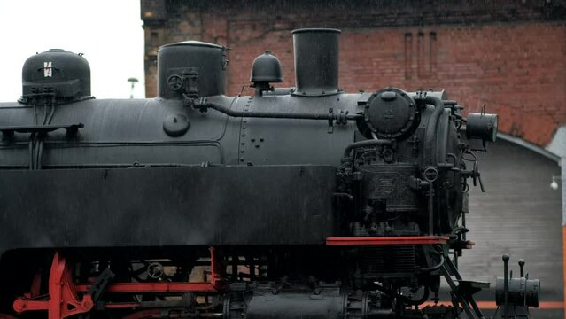 Black steam locomotive with steam propulsion system, in the rain at the museum. Close-up of the front of the locomotive.