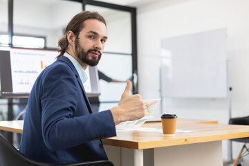 Obraz na płótnie Canvas Handsome businessman smiling with mustache beard on face showing hand thumbs up looking at camera sitting at office table. approval, achievement, satisfaction.