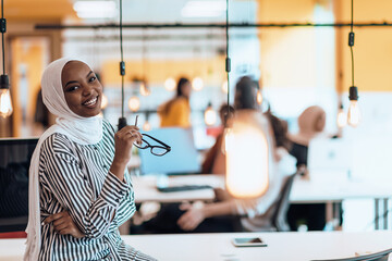 Fototapeta na wymiar Protrait of a black ( african-american) female muslim standing in a modern business office while wearing a hijab.