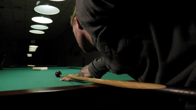 A young man playing Billiards in a club in the evening, he takes aim and prepares to hit the balls with a cue. A young man lines up his shot as he breaks the balls for the start of a game of billiards