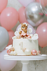 A cake on a white stand for the first birthday of a child decorated with a figurine of a bear cub and caramel candies