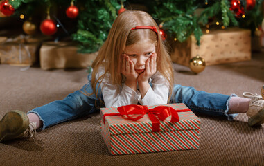 The child is sitting with sad emotions and thinking about a gift that he does not like