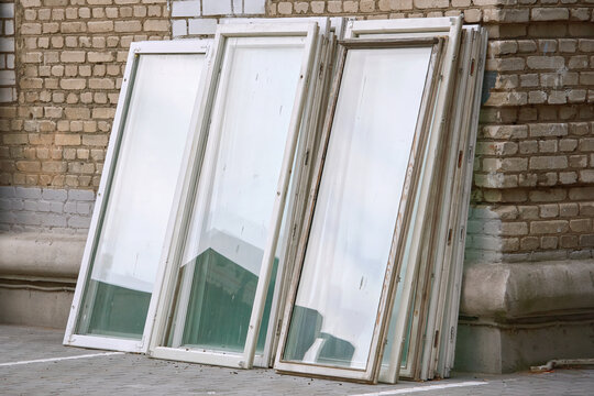 Old Wooden Window Frames With Glass Outdoors. Window Energy Saving Technology Upgrade. Old Wooden Windows Stacked Near The Building. Replacement By New Plastic Windows, Building Renovation Works.