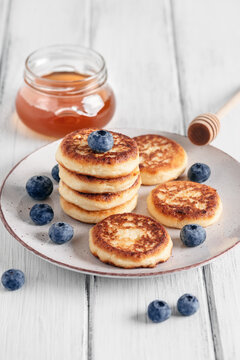 Homemade cottage cheese pancakes with blueberries and honey, white wooden old table. Side view, selective focus. Vertical image.