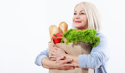 Beautiful middle-aged woman with blond hair holds products from the store in paper bag. Bread, herbs, pepper, green lettuce in her hands for a healthy diet with vitaminswith. Concept healthy food