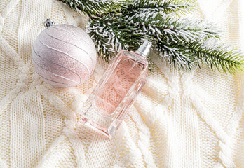 winter New Year's advertising composition of women's perfumes on a knitted beige background with a beautiful ball and a branch of spruce. - obrazy, fototapety, plakaty