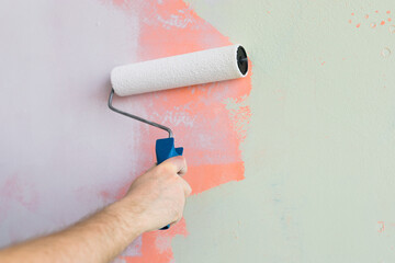 Close up man painting wall with paint roller - renovation and redecoration concept