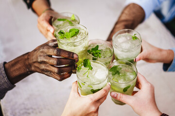 Multiethnic friends toasting outdoors with fresh mojitos cocktails sitting at table