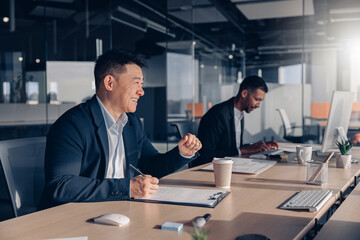 Smiling asian businessman drinking coffee while working with documents in modern office